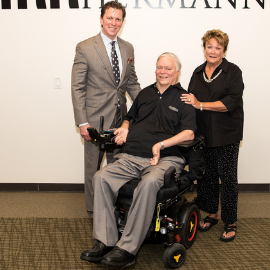 Man in a wheelchair smiles for the camera with a man and woman who are standing next to him.